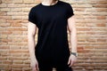 Closeup view of young muscular man wearing black tshirt and jeans posing outside. Empty brown grunge brick wall on the Royalty Free Stock Photo