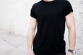Closeup view of young muscular man wearing black tshirt and jeans posing outside. Empty white wall on the background