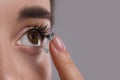 Closeup view of young woman putting contact lens in her eye against grey background. Space for text Royalty Free Stock Photo