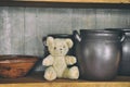 Closeup of vintage cabinet with an old teddybear sitting on a shelf with ceramic pots and bowl. Retro style