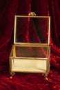 Gold and glass jewelry box with feet sits open on rich red velvet.