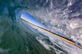 Closeup of a wave tunnel in the ocean with a person surfing and the beach in the background.