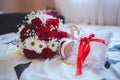 Closeup of wedding rings on a pillow with a red ribbon on a bed with a flower bouquet on it Royalty Free Stock Photo