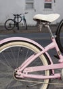 Closeup of Wheel and Seat of a Pink Framed Bicycle Parked and Locked on Street. A Blue Bicycle is in the Background