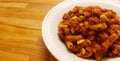 Closeup of a white bowl holding Goulashwhole wheat penne with tomato meat sauce and corn a wooden cutting board with copy space