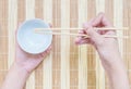 Closeup white ceramic chalice with blurred wood chopsticks in woman hand on wood mat textured background on dining table in top Royalty Free Stock Photo