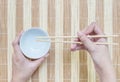 Closeup white ceramic chalice with blurred wood chopsticks in woman hand on wood mat textured background on dining table in top vi Royalty Free Stock Photo