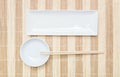 Closeup white ceramic square dish and chalice with wood chopsticks on wood mat textured background on dining table in top view Royalty Free Stock Photo