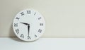 Closeup white clock for decorate show half past nine or 9:30 a.m. on white wood desk and cream wallpaper textured background with