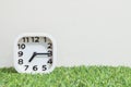 Closeup white clock for decorate show a quarter past seven or 7:15 a.m. on green artificial grass floor and cream wallpaper textur