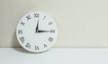 Closeup white clock for decorate show a quarter past twelve or 12:15 a.m. on white wood desk and cream wallpaper textured backgrou Royalty Free Stock Photo