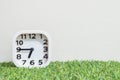 Closeup white clock for decorate show a quarter to seven or 6:45 a.m. on green artificial grass floor and cream wallpaper textured