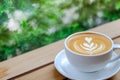 Closeup of white cup of hot coffee latte with milk foam art on wooden table with green nature background Royalty Free Stock Photo