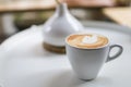 Closeup of white cup of hot coffee latte with milk foam on white round table Royalty Free Stock Photo