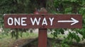 Closeup of a white font "One Way" on a brown wooden sign with an arrow pointing rightward