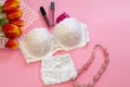 Closeup white lace woman underwear near lipstick and bouquet of red tulip flowers on pink background. Concept of beauty, passion,