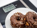 Closeup of a white plate with two delectable chocolate donuts on a weight scale Royalty Free Stock Photo