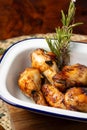 Closeup of white tray with roasted chicken wings with rosemary, on wooden table, in vertical,