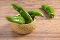 Closeup of a wicker bowl of green chili peppers on a wooden background Royalty Free Stock Photo