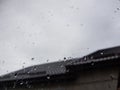 Closeup window with rain drops, blurred cloudy sky and roof of the house in background