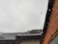 Closeup window with rain drops, blurred cloudy sky and roofs on the background