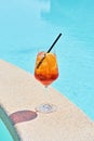 Wineglass of cold cocktail Aperol spritz against blue water of pool