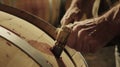A closeup of a winemakers hands expertly hammering a bung into a barrel sealing in the wine and locking it away until it