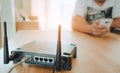 Closeup of a wireless router and a young man using a smartphone on living room at home with a window in the background . Royalty Free Stock Photo