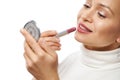 Closeup of a woman with beautiful smile applying a lipstick on her lips and looking at herself at a small cosmetic mirror Royalty Free Stock Photo