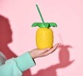 Closeup on woman hand holding pineapple shaped glass with juice or drink on her open palm over blue background Royalty Free Stock Photo