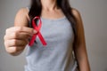 Closeup woman hand holding red ribbon HIV, world AIDS day awareness ribbon. Healthcare and medicine concept