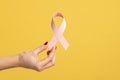 Closeup of woman hand with manicure holding pink ribbon, symbol of breast cancer awareness.