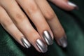 Closeup woman hand with metallic color nail polish on fingernails. Silver nail manicure with gel polish at luxury beauty salon.