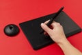 Closeup of woman hand, stylus and black graphics tablet on the red surface.Colorful creativity