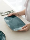 Woman holding empty blue rectangular dish on table with silver cutlery