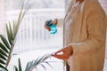 Closeup of woman hands pouring water from sprinkler on green home plant. Large houseplant howea palm in apartment house interior