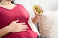 Woman having stomachache or flatulence after eating burger, hand holding her abdominal