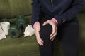 Woman wearing black sport pants and hoody, sitting on the sofa and holding her knee.Concept of sport pain in the knee Royalty Free Stock Photo