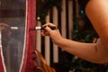 Closeup of woman painting carved ornaments on door with glass of antique cupboard made of wood in pink color. Giving new