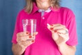 Closeup of a woman in a pink shirt holding a glass of water and a pill against blue background Royalty Free Stock Photo