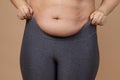 Closeup of woman putting on leggings with flabby large abdomen on beige background. Body positive. Violation of cell