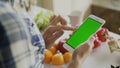 Closeup of woman`s hand browsing smartphone with green screen on kitchen at home Royalty Free Stock Photo