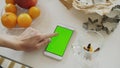 Closeup of woman`s hand browsing smartphone with green screen on kitchen table at home Royalty Free Stock Photo