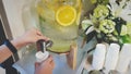 Closeup woman`s hand dispense water from a large glass jug with fresh sliced lemon inside in vintage tone.