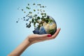 Closeup of woman`s hand holding Earth which is breaking into small pieces that are flying away on light blue background. Royalty Free Stock Photo