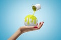 Closeup of woman`s hand holding white tennis ball on palm and small can of yellow paint in air pouring paint onto ball Royalty Free Stock Photo