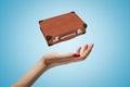 Closeup of woman`s hand levitating brown travel case on light blue background.