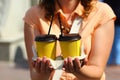 Closeup of woman`s hands holding two corrugated yellow plastic coffee cups. mockup,