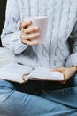 Closeup of woman`s hands in sweater holding book and cup of warm tea Royalty Free Stock Photo