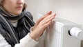 Closeup of woman in scarf warming hands at heating radiator in house. Concept of energy crisis, high bills, broken heating system Royalty Free Stock Photo